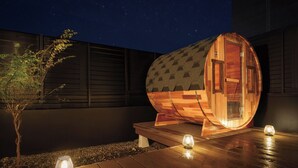 A wooden sauna structure with a curved roof, a door labeled 'SAUNA,' and a small table with a candle. - Ishigaki sen (Beppu)