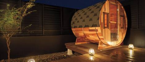 A wooden sauna structure with a curved roof, a door labeled 'SAUNA,' and a small table with a candle.