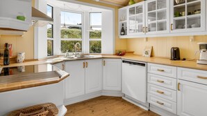 Une cuisine moderne avec des meubles blancs, un plan de travail en bois et une vue sur l’extérieur grâce à de grandes fenêtres.