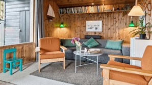 A cozy room with wooden walls, a sofa, two armchairs, a coffee table, and a bookshelf filled with books.