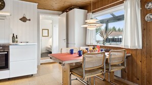 A modern kitchen with white cabinets, a wooden ceiling, and a dining area with wicker chairs and a red table.