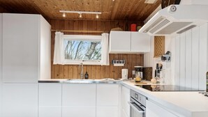 A modern kitchen with white cabinets, a wooden ceiling, and a window overlooking trees.