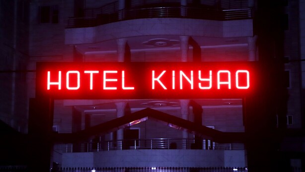 Une enseigne au néon indiquant « HÔTEL KINYAO » sur un immeuble moderne.