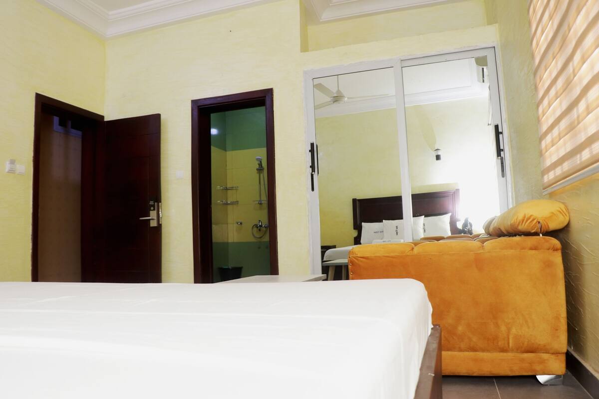 A hotel room with a bed, a sofa, a bathroom with a shower, and a wardrobe.