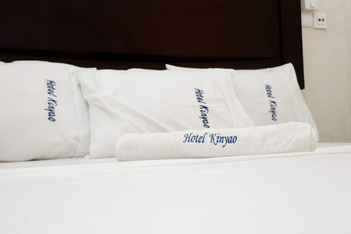 A neatly made bed with white pillows and a folded towel, each labeled "Hotel Kinyango."