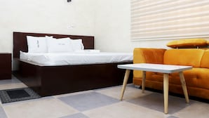 Une chambre d’hôtel avec un lit, une petite table, un canapé et une fenêtre avec des stores.