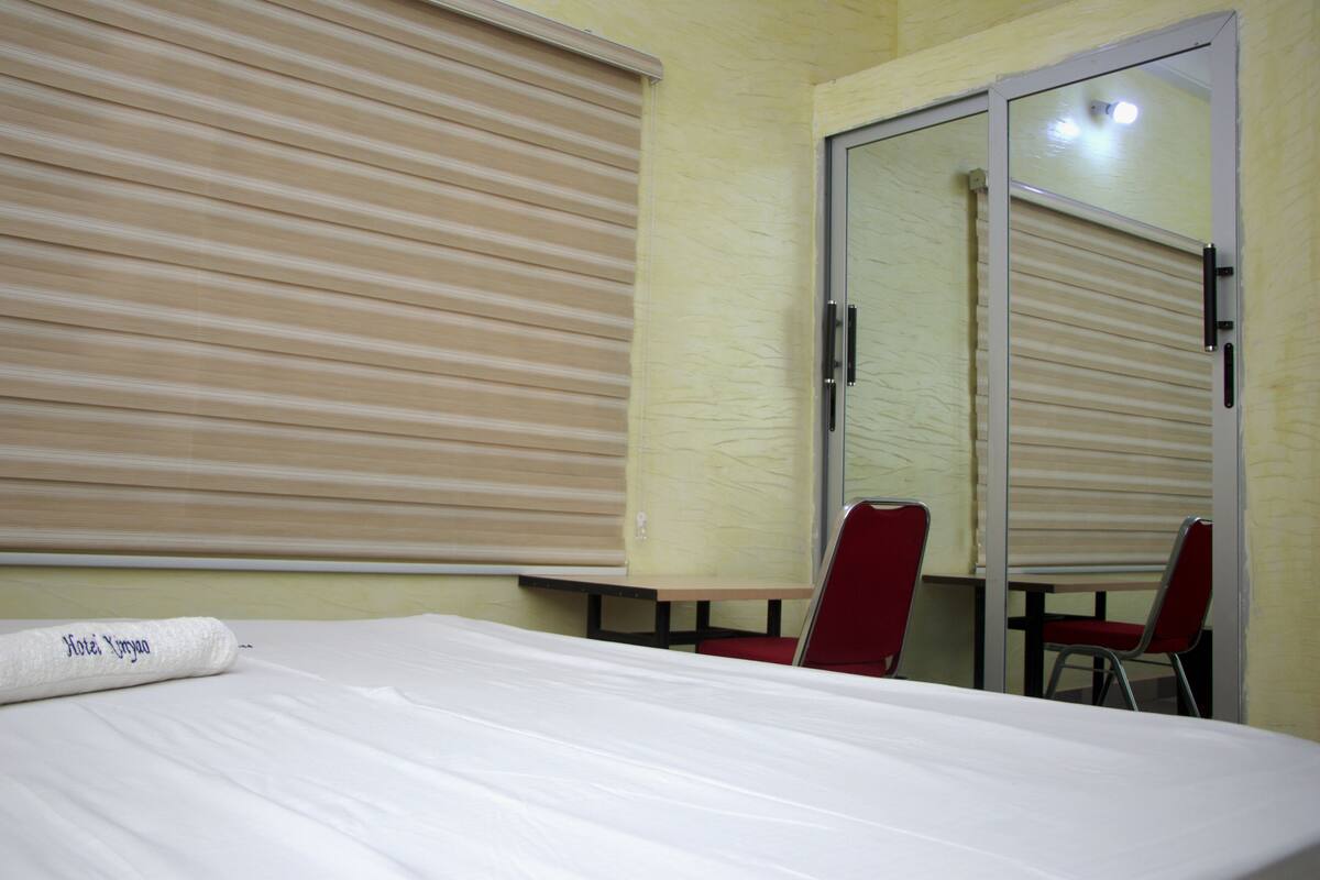 A hotel room with a bed, a table, and two red chairs.
