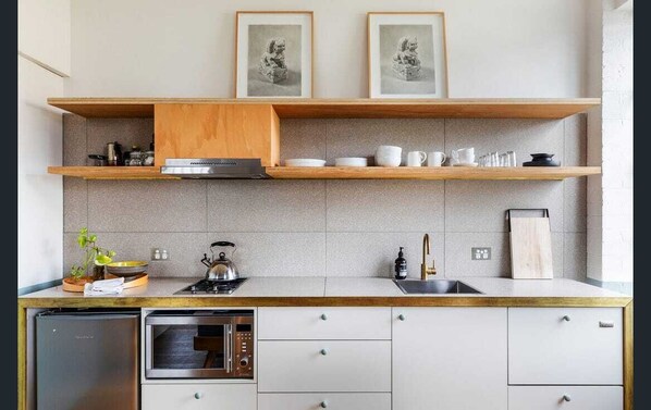 A modern kitchen with a built-in dishwasher, oven, and microwave. There are wooden shelves above the counter holding dishes and a framed picture.