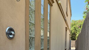 Un estrecho sendero de concreto bordeado por un edificio color crema con ventanas amplias y una cerca de madera.