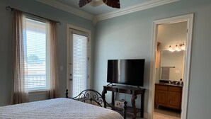 Un dormitorio con cama, televisor sobre un mueble de madera y baño visible a través de una puerta abierta.
