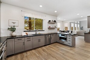 A modern kitchen with grey cabinets, a large island, and a window with a view of trees. - *Monthly Rental*Modern Home *Fenced Yard*Near NAU (Flagstaff)