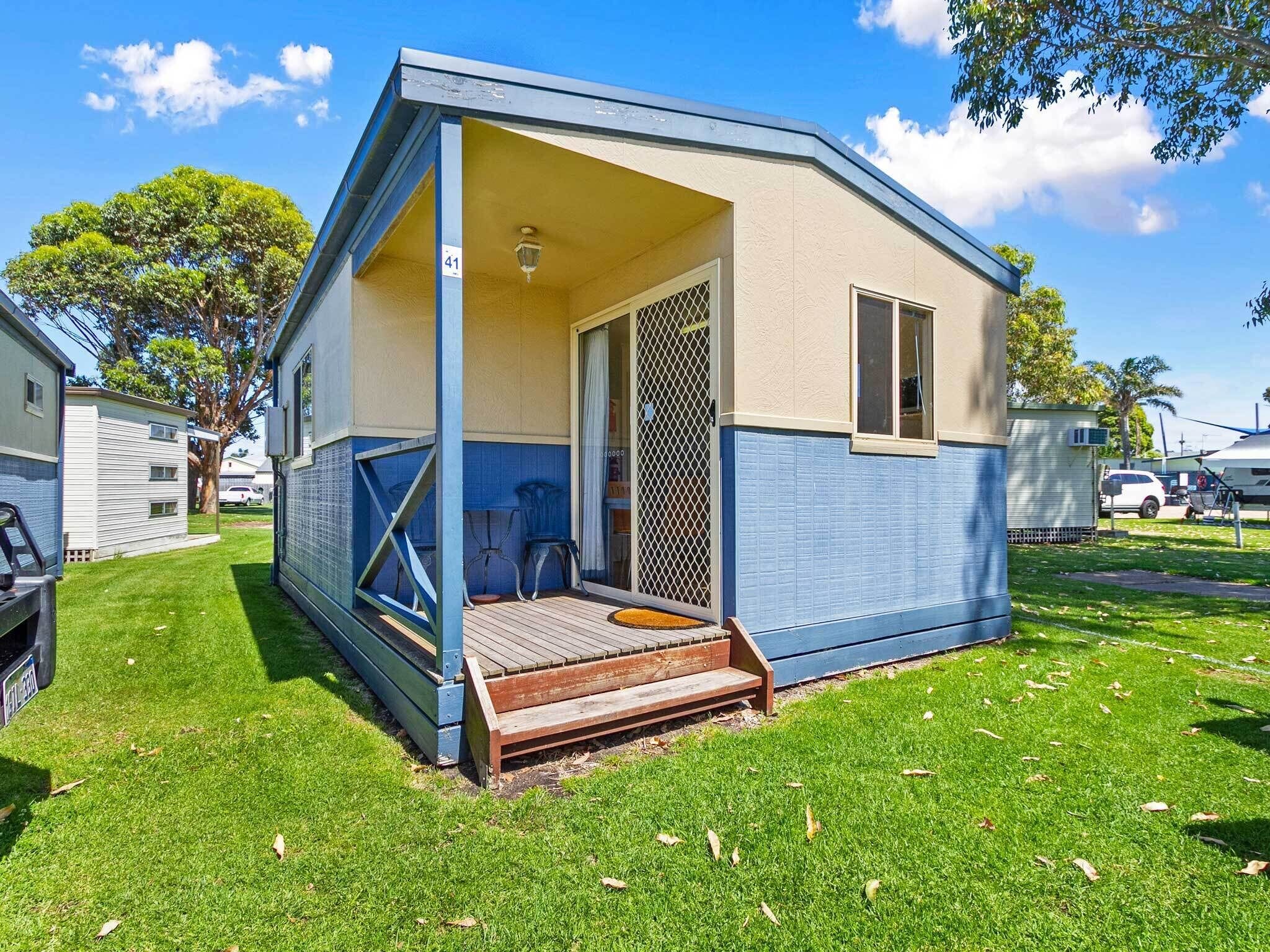 Uma casa móvel pequena, térrea, com varanda, uma janela e uma porta com tela.