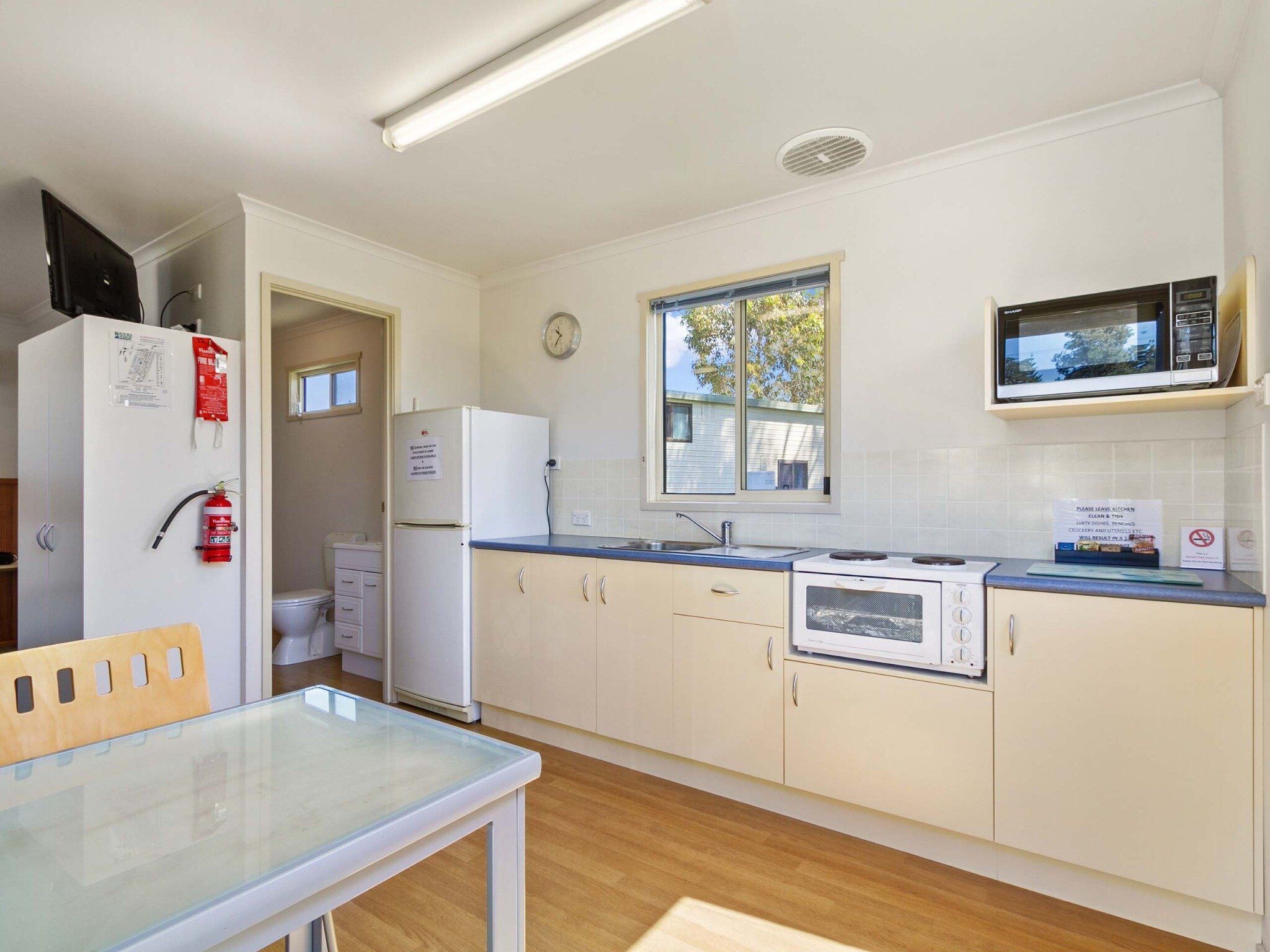 Una cocina compacta con armarios blancos, microondas, estufa y ventana que deja entrar luz natural.