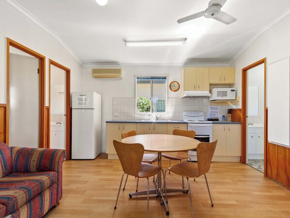 Una cocina compacta con electrodomésticos blancos, una mesa de comedor con cuatro sillas y un ventilador de techo.
