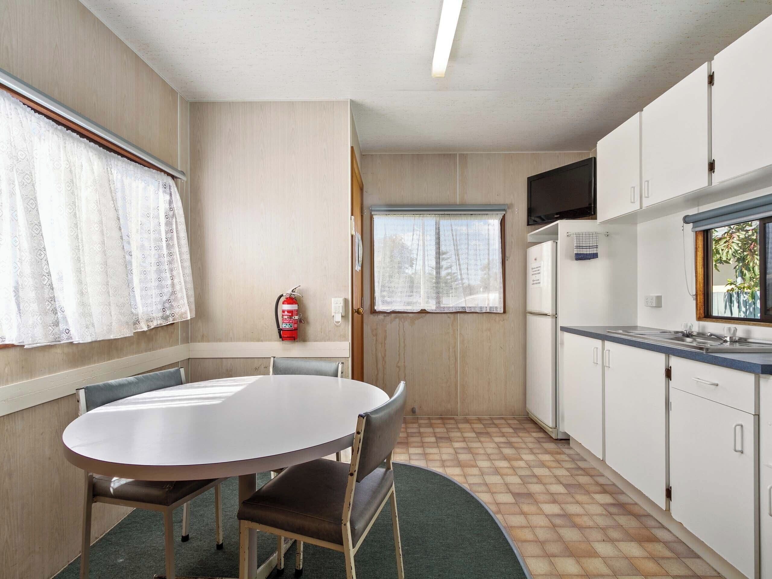 Cocina compacta con una mesa y sillas, un extintor, una ventana y un televisor.