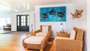 Ein Zimmer mit Holzboden, zwei gewebte Sessel, eine weiße Wand mit einem blauen Gemälde von Meeresschildkröten und eine Holztür.