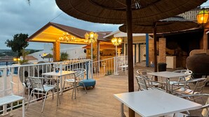 An outdoor dining area with tables and chairs, a thatched roof, and a view of the sea. - Quinta Jardim das Palmeiras, T2 nº3, Algoz (Silves)