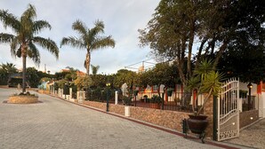 A paved courtyard with palm trees, a stone wall, and a gated entrance. - Quinta Jardim das Palmeiras, T2 nº3, Algoz (Silves)