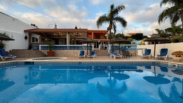 A swimming pool with lounge chairs and umbrellas, surrounded by a building with a tiled roof and a stone wall. - Quinta Jardim das Palmeiras, T2 nº3, Algoz (Silves)