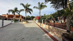 A paved walkway with hexagonal tiles, bordered by a low stone wall and a metal fence. - Quinta Jardim das Palmeiras, T2 nº6, Algoz (Silves)