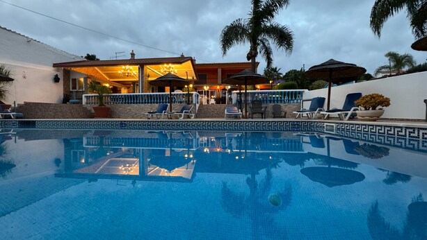 A swimming pool with lounge chairs and umbrellas, a covered patio area, and a stone wall. - Quinta Jardim das Palmeiras, T2 nº6, Algoz (Silves)