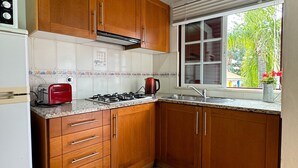 A kitchen with wooden cabinets, a gas stove, a red toaster, and a window with a view of greenery.