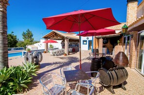 Relax in a patio area with a pool view, featuring a dining table and comfortable seating under a shaded umbrella.