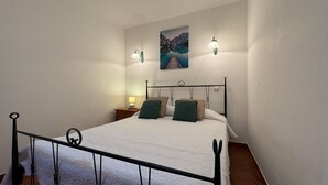 Une chambre à coucher avec un lit, deux lampes fixées au mur, une table de chevet et un tableau représentant un lac.