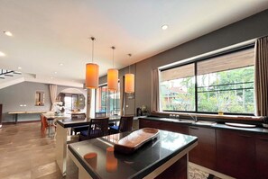 Uma cozinha moderna com uma janela ampla, luminárias pendentes e um espaço de jantar com um banco.