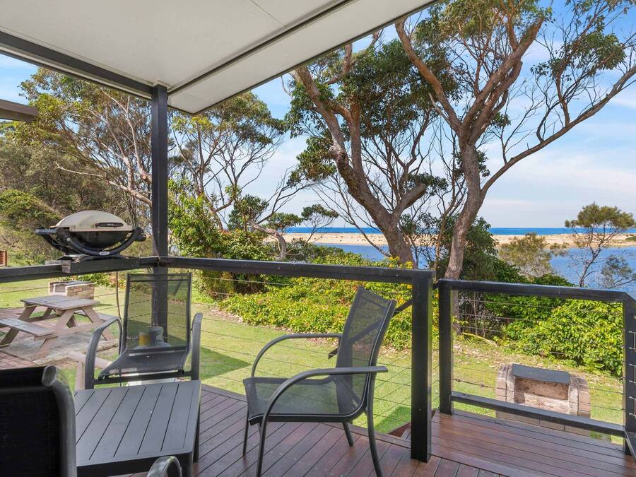 A deck with outdoor seating, a grill, and a view of the beach and ocean.