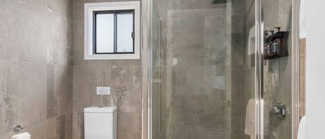 A modern bathroom with a glass-enclosed shower, a toilet, and a window above the toilet.