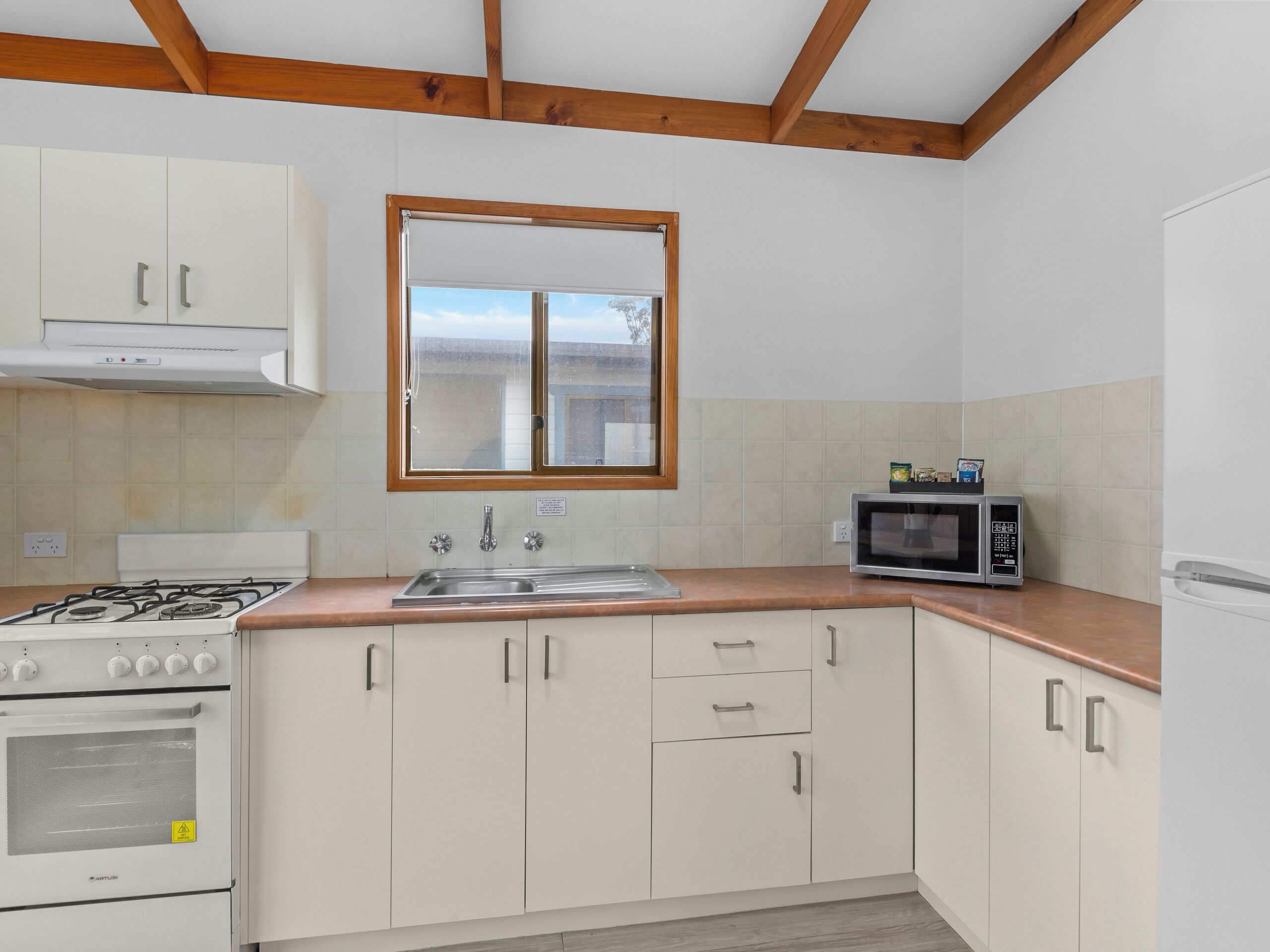 Una cocina con armarios blancos, estufa, microondas y ventana sobre el fregadero.