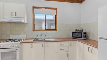 Una cocina con armarios blancos, estufa, microondas y ventana sobre el fregadero.
