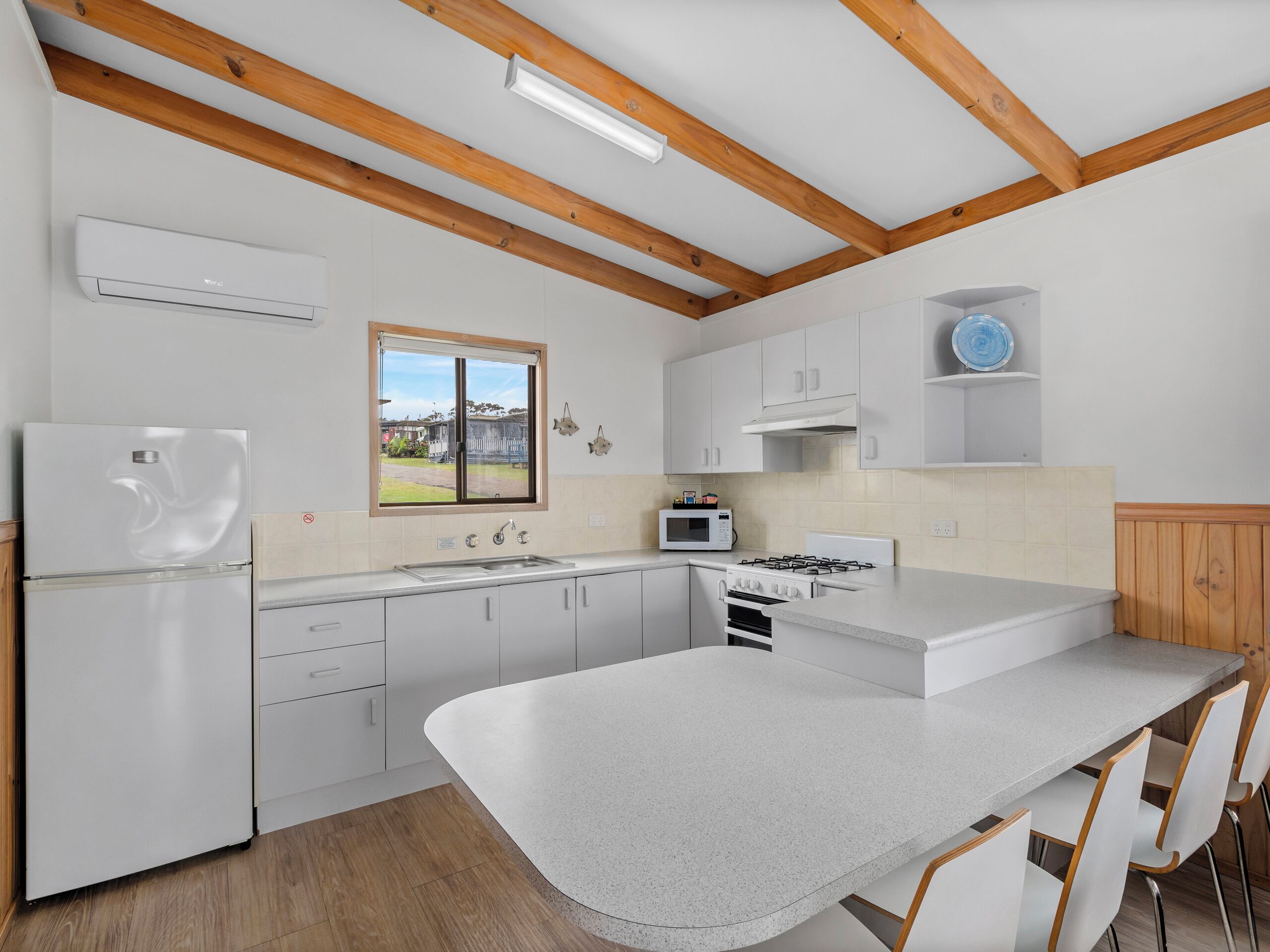 A modern kitchen with white cabinets, a stainless steel refrigerator, a built-in oven, and a large island with bar stools.