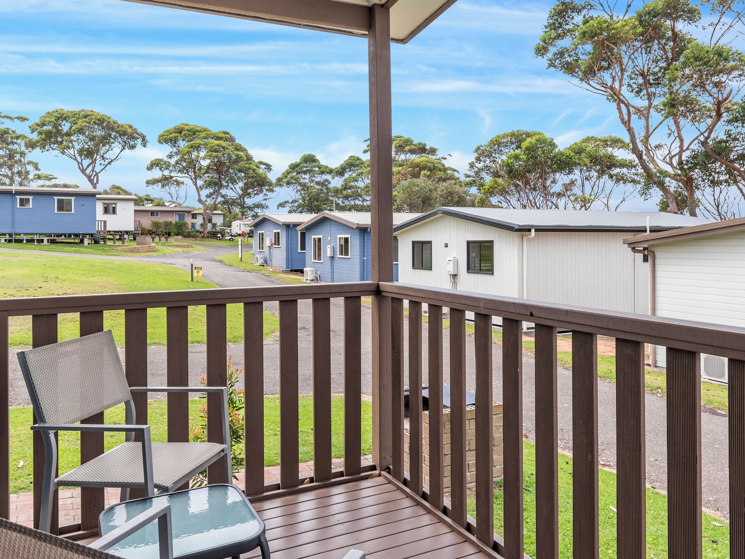 A deck with a chair and table, overlooking a campground with mobile homes and trees.