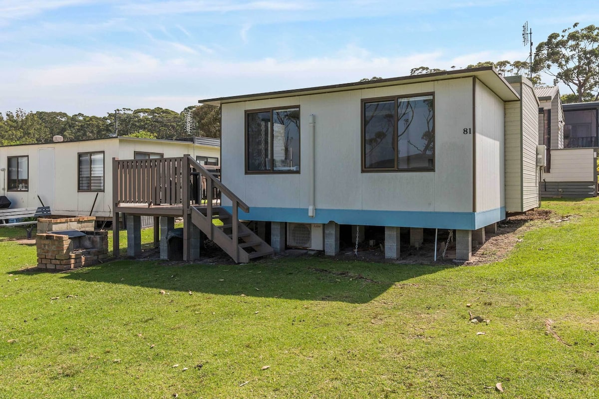A mobile home with a blue base, a wooden deck, and a staircase leading to the entrance.