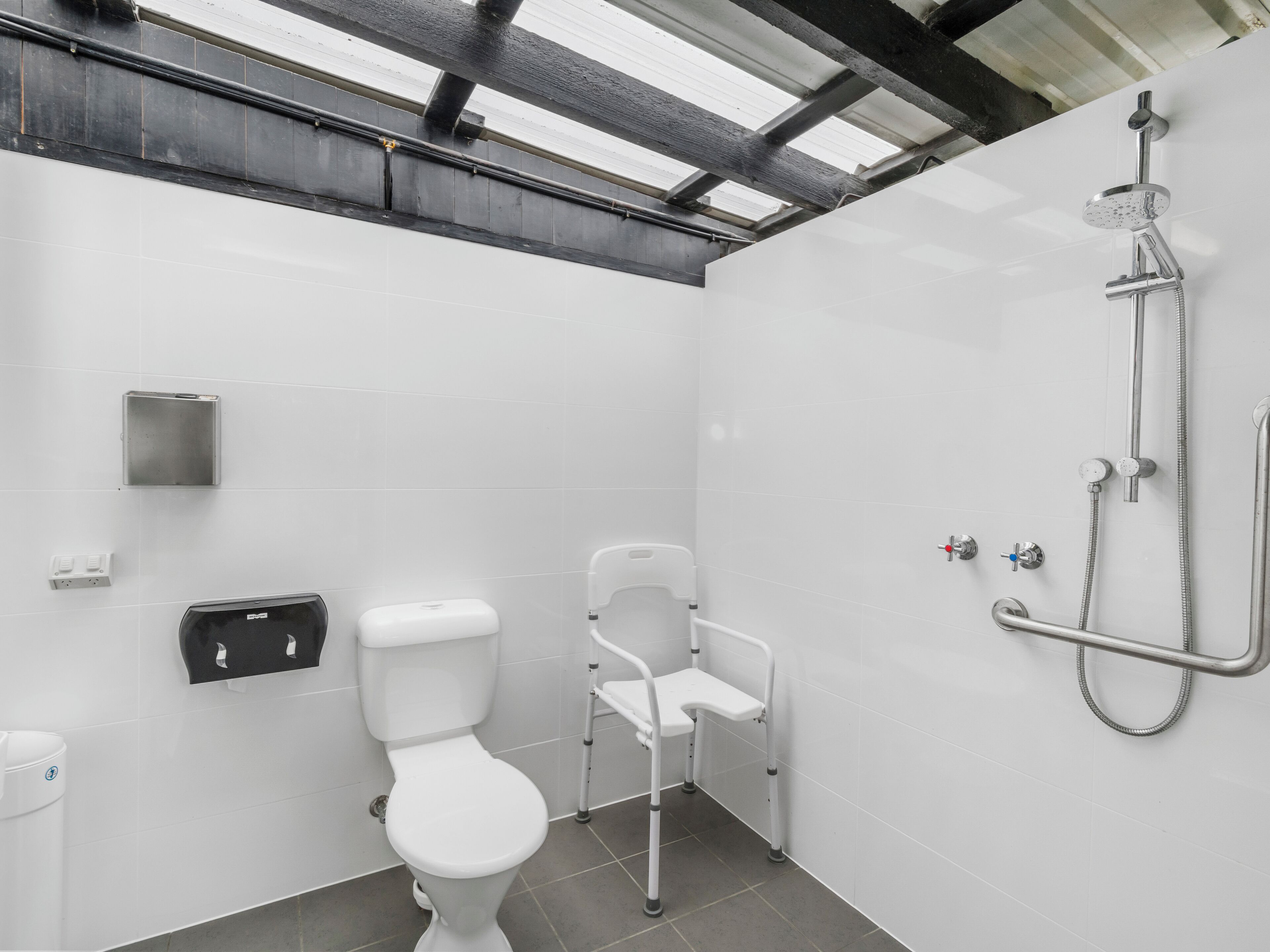 Ein modernes Badezimmer mit Toilette, Handtrockner, Seifenspender und Dusche mit Duschbrause und Brauseschlauch.