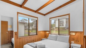 Une chambre à coucher avec un grand lit, des murs en bois et deux fenêtres donnant sur l’extérieur.