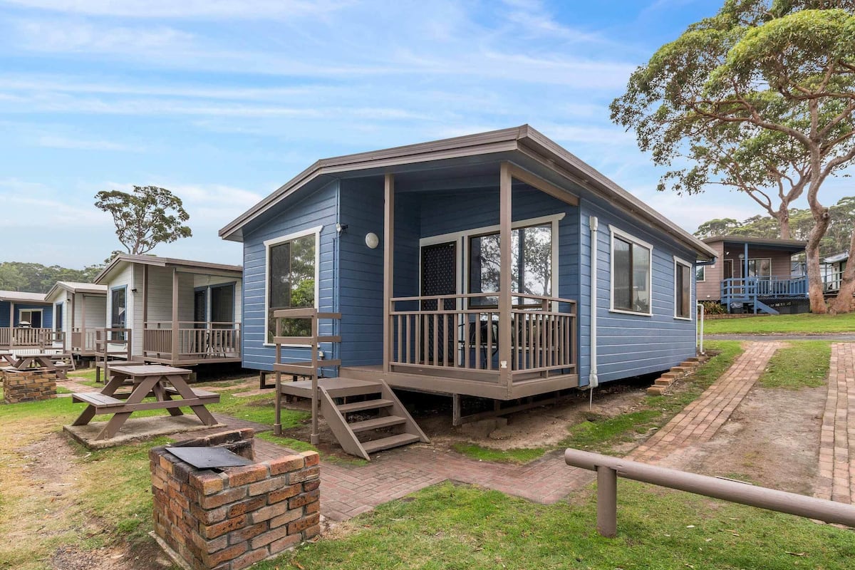 A blue mobile home with a porch, a brick fireplace, and a picnic table.