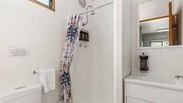 A bathroom with a shower, toilet, and sink. There is a towel hanging on the toilet, a shower curtain, and a mirror above the sink.