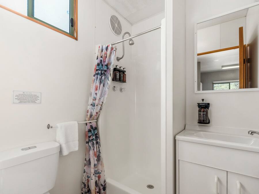 A bathroom with a shower, toilet, and sink. There is a towel hanging on the toilet, a shower curtain, and a mirror above the sink.