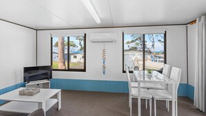 Une pièce aux couleurs blanche et bleue, dotée d’un téléviseur à écran plat, d’une table à manger avec des chaises et de grandes fenêtres offrant une vue sur l’extérieur.