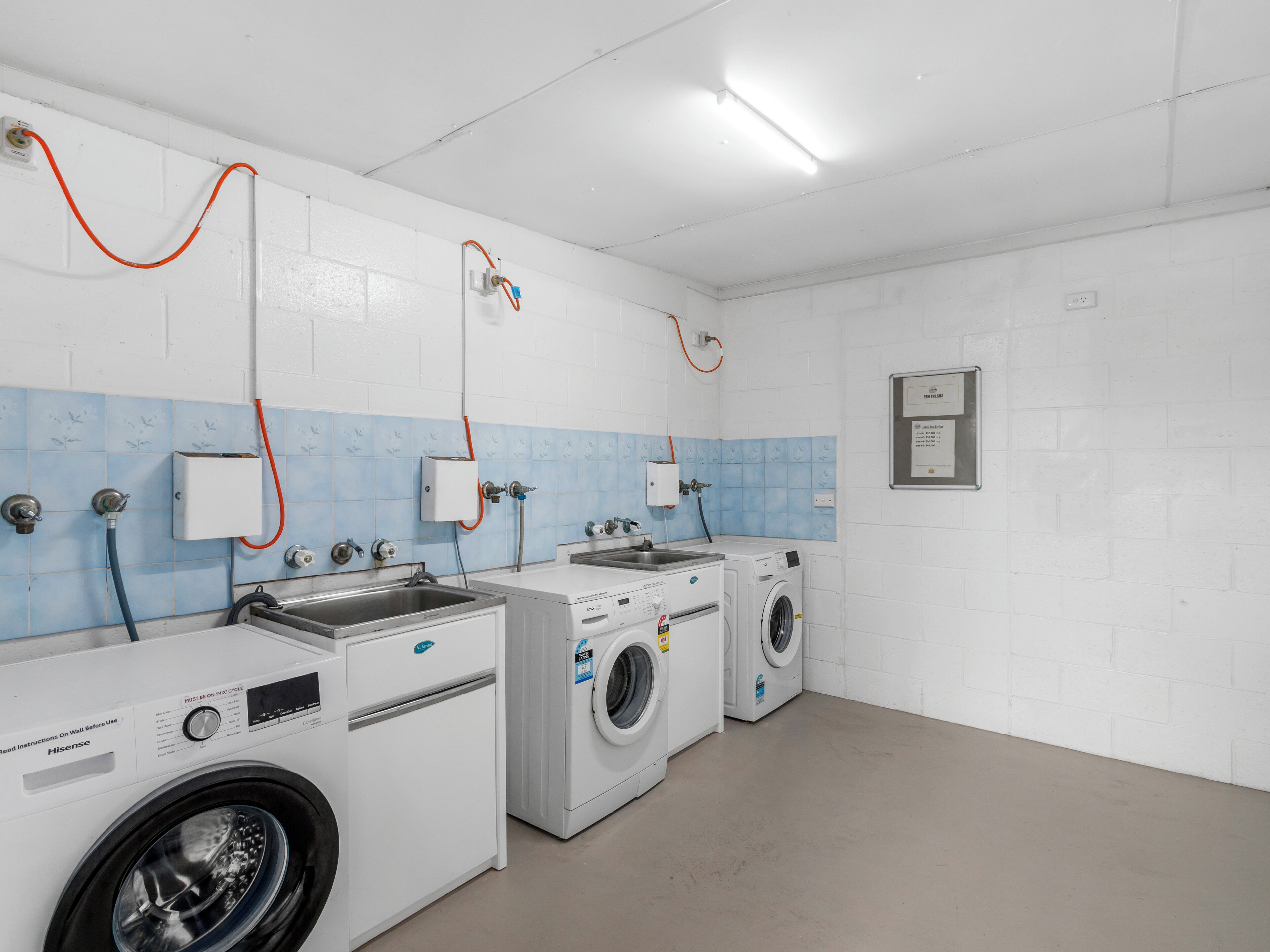 A laundry facility with two washing machines and two sinks, equipped with hoses and a control panel.