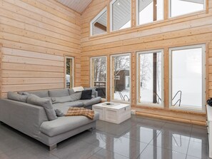 L’intérieur d’un chalet moderne en bois, avec un canapé gris, une table basse blanche et de grandes fenêtres donnant sur un paysage enneigé.