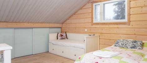 Een slaapkamer met een schuine kap, een raam, een bed met bloemenbedekking, een nachtkastje en een dressingkast.