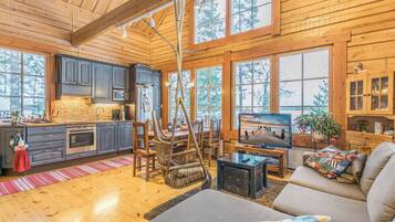 Een ruim interieur van een chalet met een keuken, eethoek en woonkamer, met houten wanden en grote ramen.