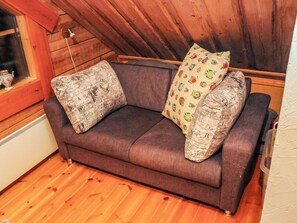 Un canapé marron avec des coussins à motifs, dans une pièce dotée d’un plancher en bois et d’un plafond en pente.