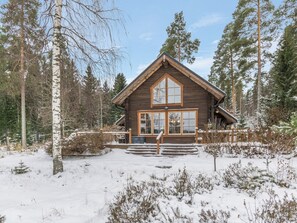 A wooden cabin with a steep roof, large windows, and a snow-covered landscape.
