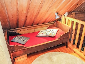 Una cama de madera pequeña con un colchón rojo, una almohada y una lámpara sobre una mesita de noche de madera.