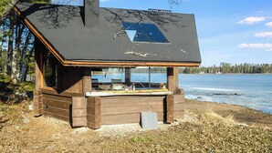 Une cabane en bois avec une grande fenêtre, une cheminée et une vue sur un lac.